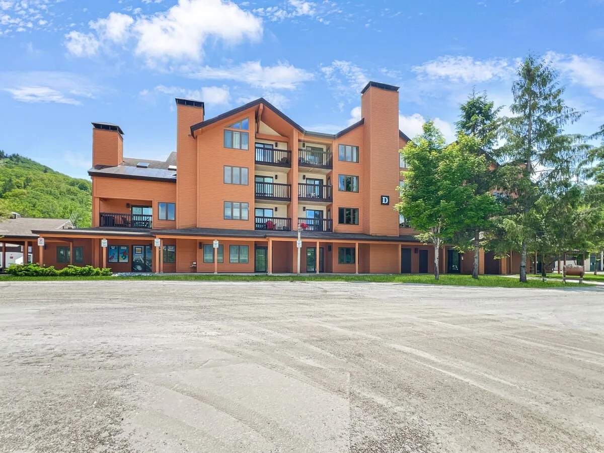The hero image displays the exterior of the condo building nestled among lush trees, with balconies overlooking the scenic surroundings. The scene captures a warm, inviting atmosphere at sunset, highlighting the private balconies and the natural beauty of the area, suggestive of relaxation, outdoor gatherings, and easy access to nature.