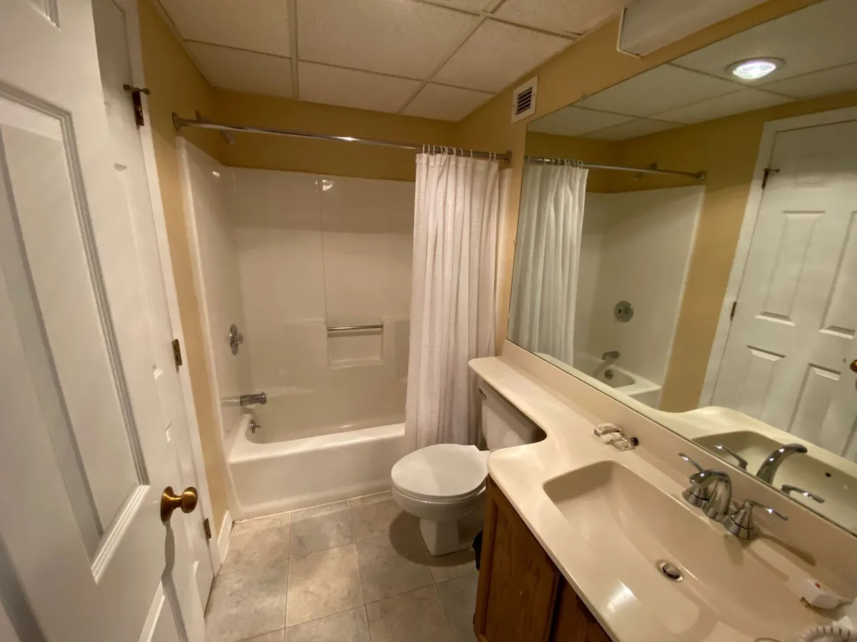 This photo captures a well-appointed full bathroom, featuring a bathtub, sink, mirror, and toilet. The space is practical yet serene, offering a calming place to unwind after an active day.