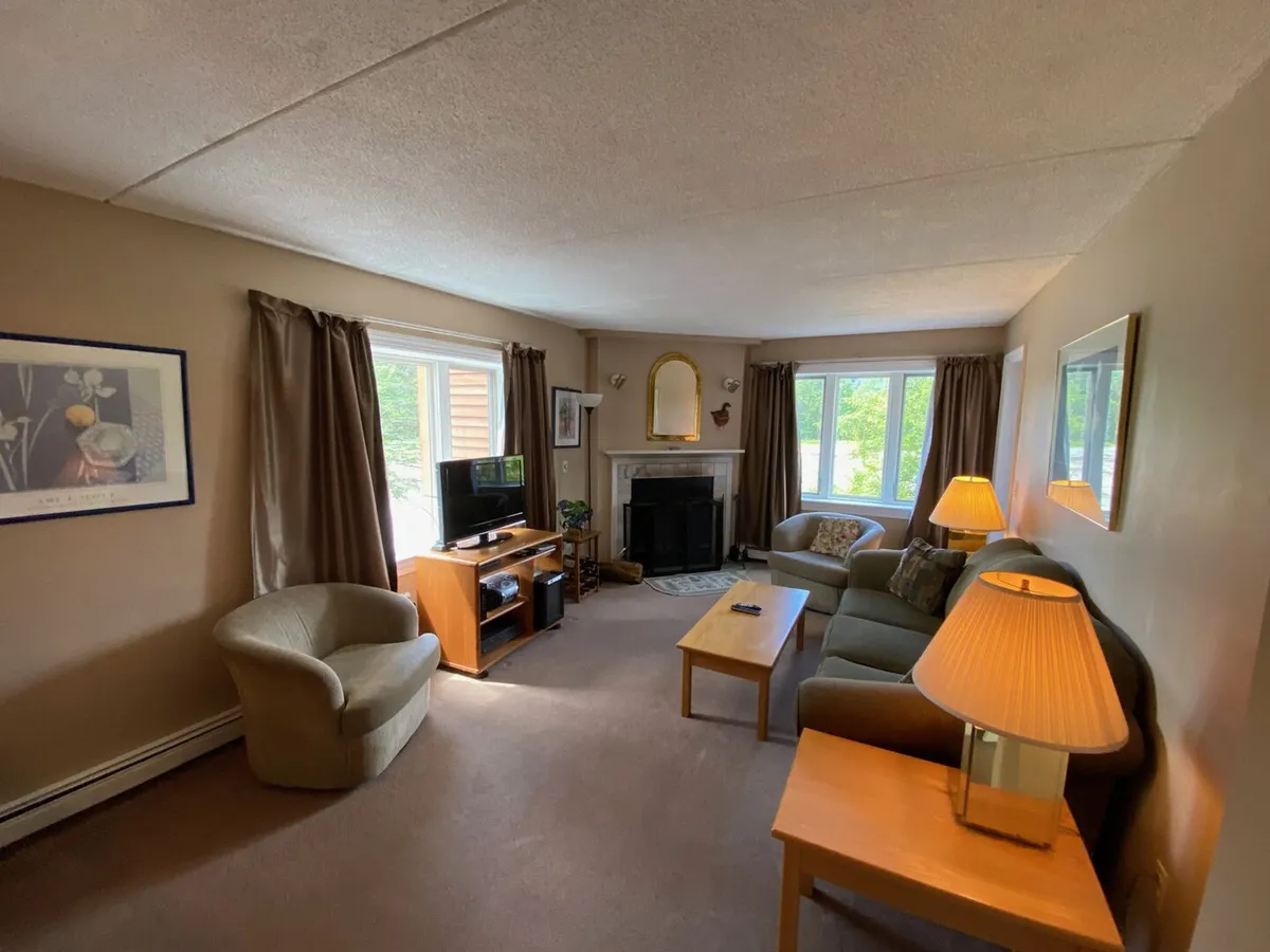 A stylish and welcoming living area with a plush sofa, an armchair, a coffee table, and a modern fireplace. Large windows invite in soft daylight, creating a restful environment for relaxation and socializing.