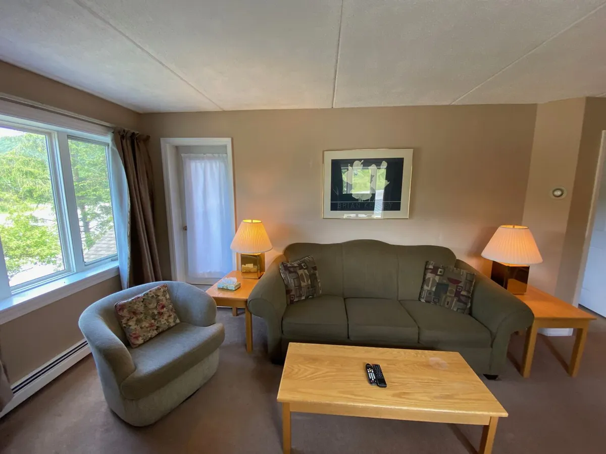 A cozy sitting area featuring a comfortable sofa, an accent chair, warm lighting from table lamps, and a window with tranquil views. The space evokes a sense of calm, perfect for quiet moments after a workout or yoga class.
