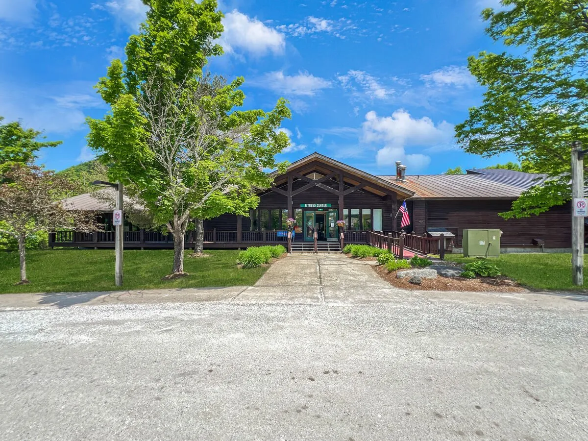 This image shows the main entrance to the building, framed by lush greenery and a flagpole. The scene is bright and inviting, suggesting a vibrant community and easy entry for guests eager to hit the slopes.